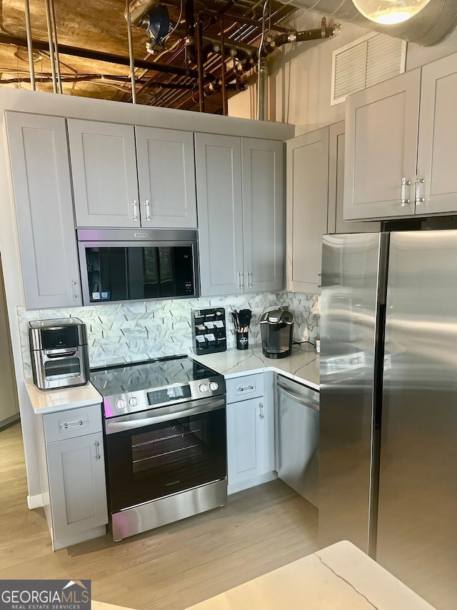 kitchen with tasteful backsplash, gray cabinetry, light wood-type flooring, and appliances with stainless steel finishes