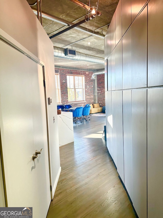 hallway with light hardwood / wood-style flooring and brick wall