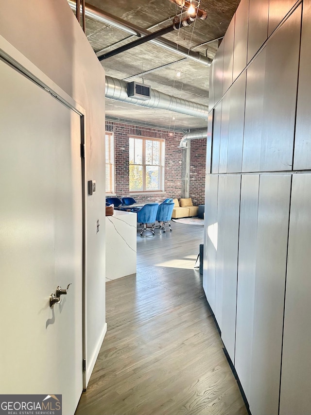 hallway featuring light hardwood / wood-style flooring and brick wall