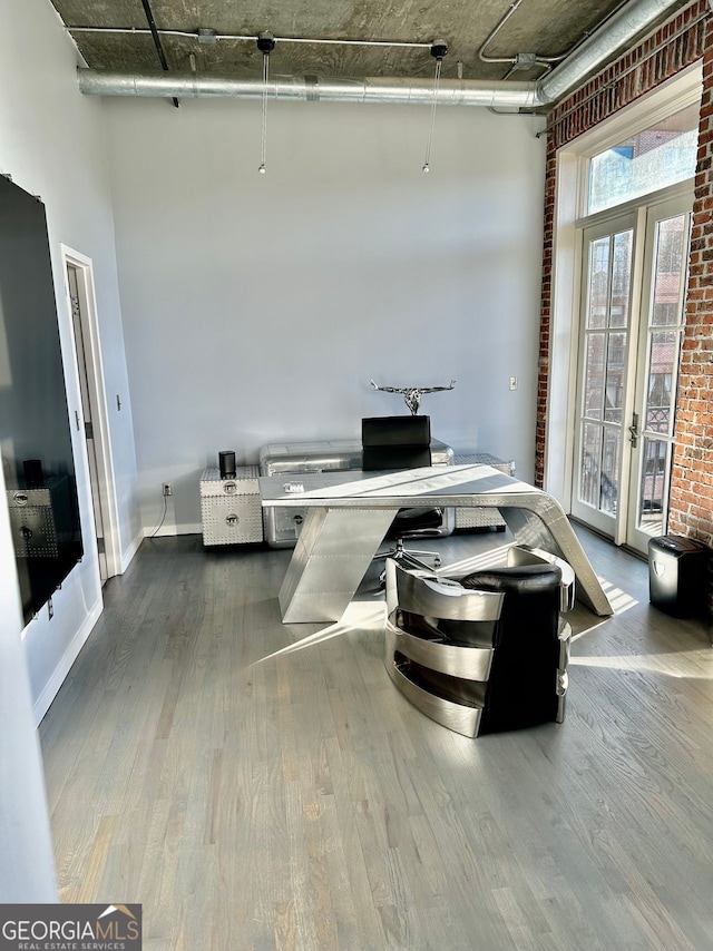 office space featuring hardwood / wood-style flooring, a towering ceiling, brick wall, and french doors