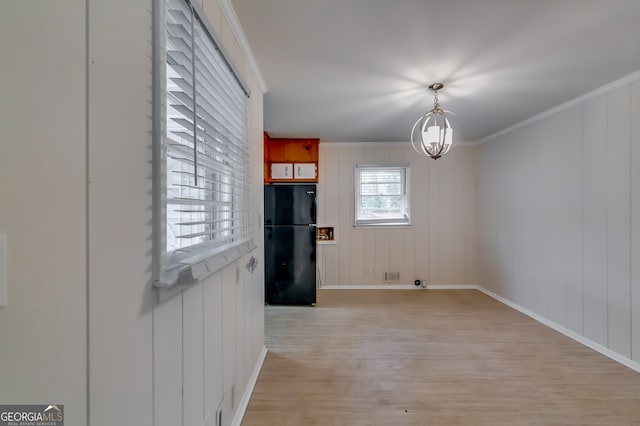 unfurnished dining area with crown molding, an inviting chandelier, and light wood-type flooring