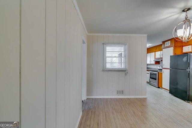 kitchen featuring stainless steel range with electric cooktop, a chandelier, black refrigerator, ornamental molding, and light hardwood / wood-style floors