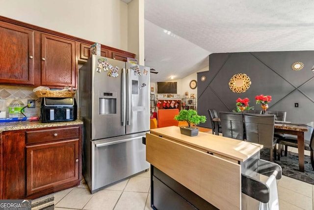 kitchen with stainless steel fridge, light tile patterned floors, tasteful backsplash, and vaulted ceiling