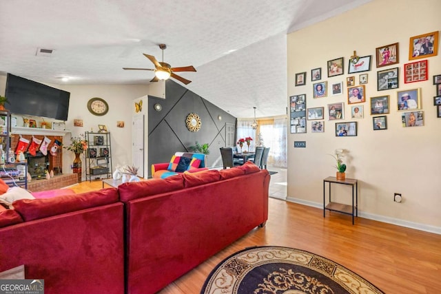 living room featuring light wood-type flooring, a textured ceiling, ceiling fan, a fireplace, and lofted ceiling