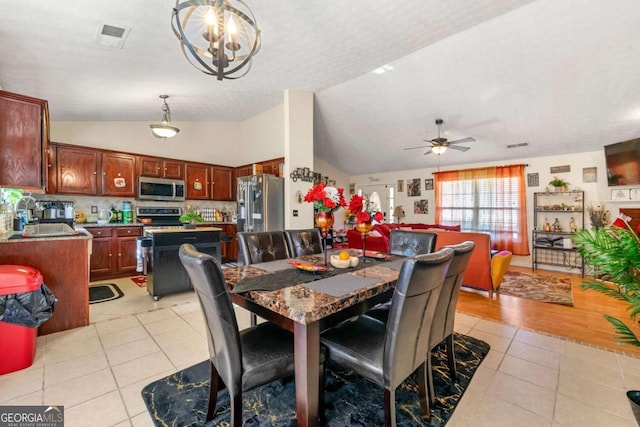 dining space with light tile patterned floors, ceiling fan with notable chandelier, vaulted ceiling, and sink