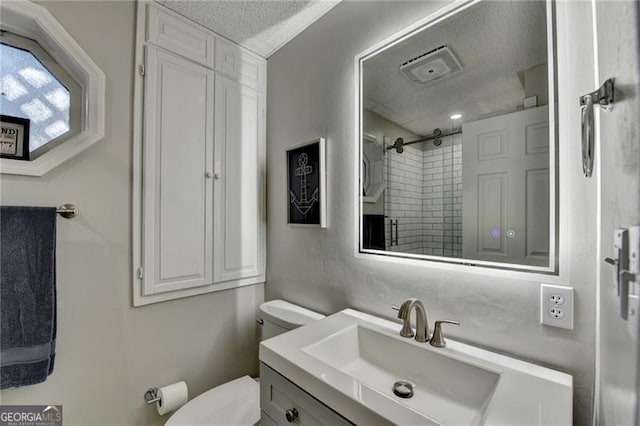 bathroom featuring a textured ceiling, vanity, a tile shower, and toilet