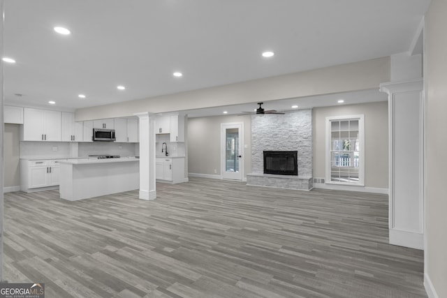 unfurnished living room with light wood-type flooring, a stone fireplace, and ceiling fan