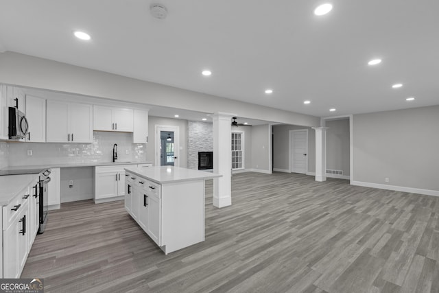 kitchen featuring a center island, backsplash, a fireplace, appliances with stainless steel finishes, and white cabinetry