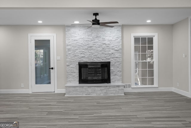 unfurnished living room with a stone fireplace, ceiling fan, and hardwood / wood-style floors