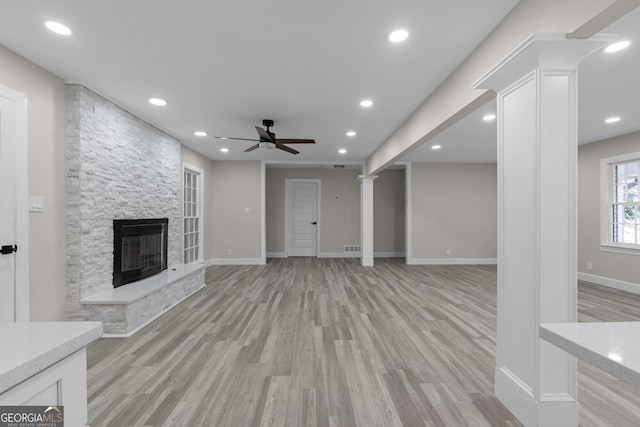 unfurnished living room featuring ceiling fan, light hardwood / wood-style floors, a fireplace, and decorative columns