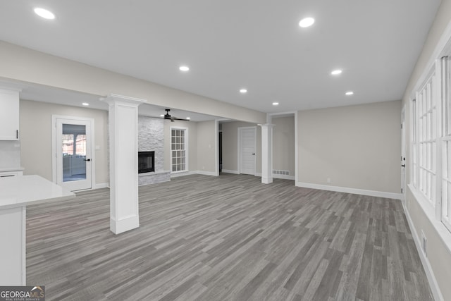 unfurnished living room with ceiling fan, a stone fireplace, and light hardwood / wood-style flooring