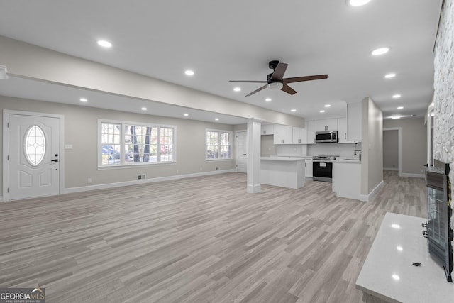 unfurnished living room with a stone fireplace, ceiling fan, sink, and light hardwood / wood-style floors