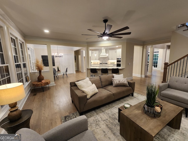 living room with ceiling fan with notable chandelier, light hardwood / wood-style floors, and ornamental molding