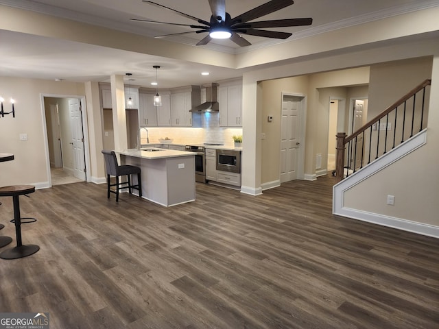 kitchen with wall chimney exhaust hood, hanging light fixtures, crown molding, a kitchen island with sink, and appliances with stainless steel finishes