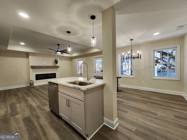 kitchen with light stone countertops, sink, dishwasher, hanging light fixtures, and dark wood-type flooring