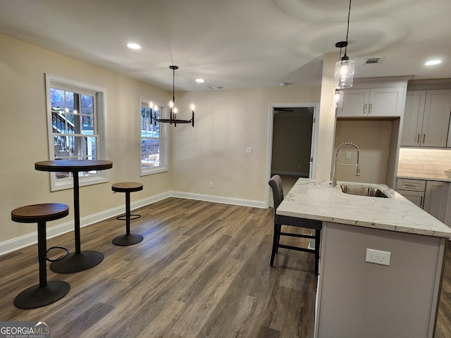 kitchen featuring light stone countertops, sink, dark hardwood / wood-style floors, hanging light fixtures, and an island with sink