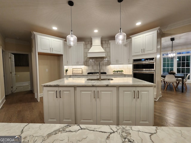 kitchen with decorative light fixtures, white cabinetry, light stone countertops, and custom range hood