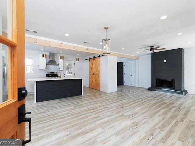 living room with light wood-type flooring, a barn door, ceiling fan, and a fireplace