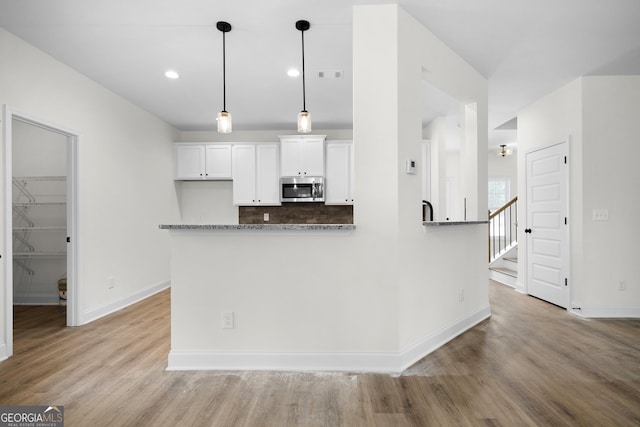 kitchen with tasteful backsplash, white cabinetry, light hardwood / wood-style flooring, and pendant lighting