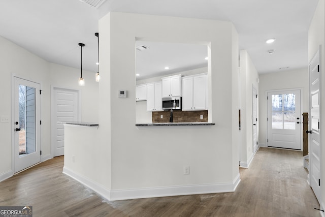 kitchen featuring dark stone counters, white cabinets, light wood-type flooring, decorative light fixtures, and kitchen peninsula