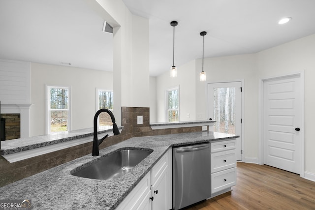 kitchen featuring stainless steel dishwasher, sink, hardwood / wood-style flooring, dark stone countertops, and white cabinetry