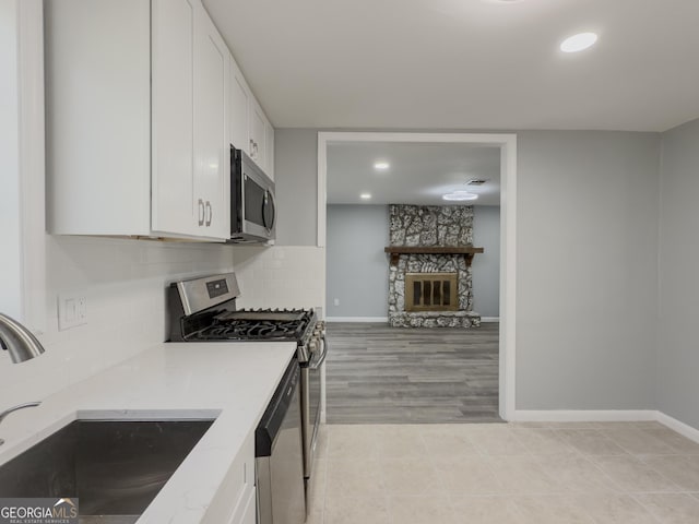 kitchen with sink, stainless steel appliances, a stone fireplace, light hardwood / wood-style flooring, and white cabinets