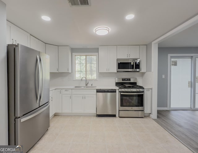 kitchen with sink, white cabinetry, stainless steel appliances, and light hardwood / wood-style flooring