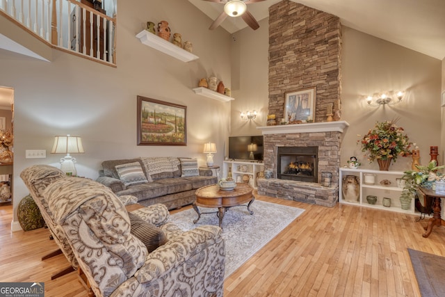 living room featuring high vaulted ceiling, ceiling fan, light hardwood / wood-style flooring, and a stone fireplace