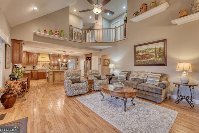 living room with light wood-type flooring, a towering ceiling, and ceiling fan with notable chandelier