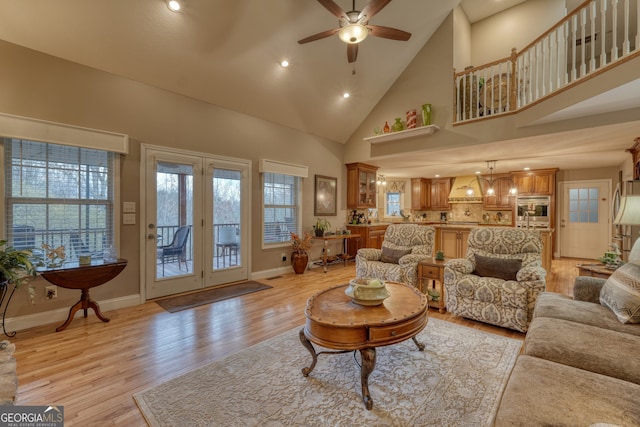 living room with light hardwood / wood-style floors, high vaulted ceiling, and ceiling fan with notable chandelier