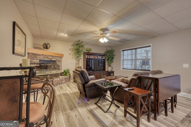 living room featuring a paneled ceiling, a stone fireplace, ceiling fan, and light hardwood / wood-style flooring