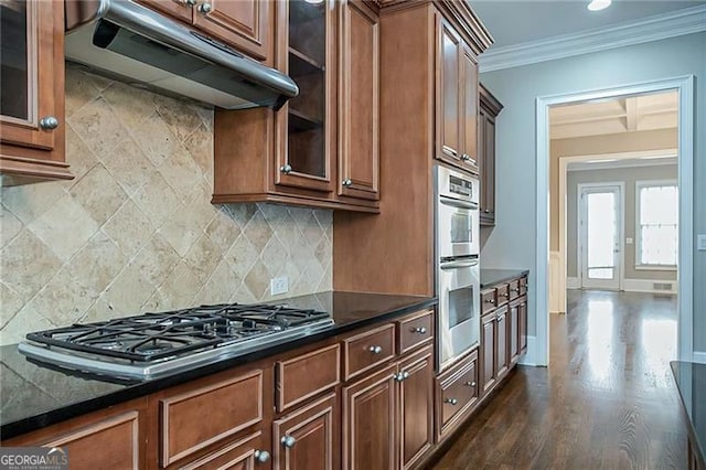 kitchen with crown molding, dark hardwood / wood-style floors, decorative backsplash, dark stone countertops, and stainless steel appliances