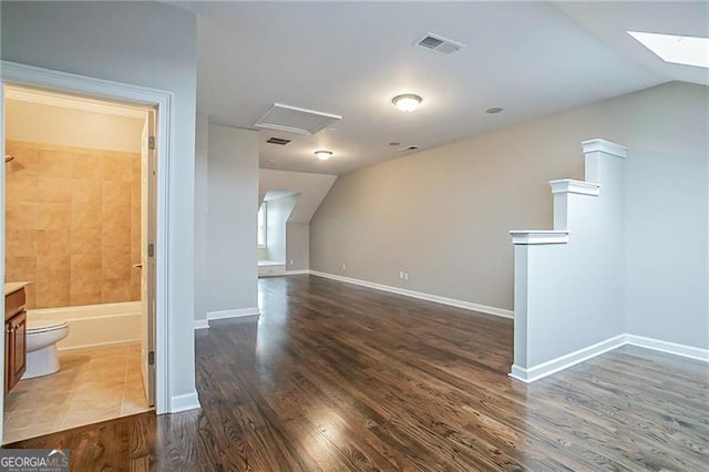 additional living space with vaulted ceiling with skylight and dark hardwood / wood-style flooring