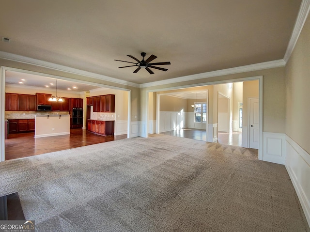 unfurnished living room featuring dark colored carpet, ceiling fan with notable chandelier, and ornamental molding