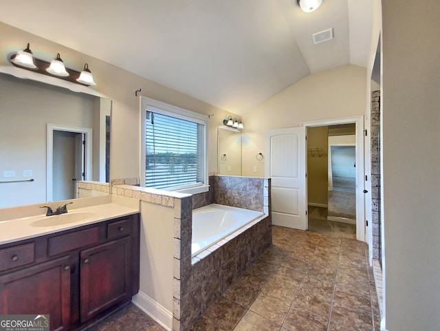 bathroom with tile patterned floors, vanity, tiled bath, and vaulted ceiling