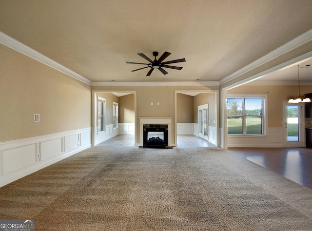 unfurnished living room with a multi sided fireplace, carpet floors, ceiling fan with notable chandelier, and crown molding