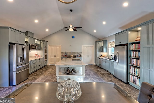 kitchen featuring light stone counters, stainless steel appliances, ceiling fan, sink, and a center island