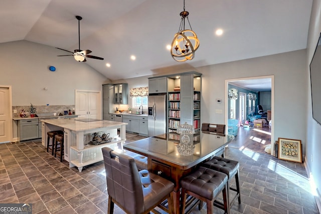 dining space featuring ceiling fan with notable chandelier, vaulted ceiling, and sink