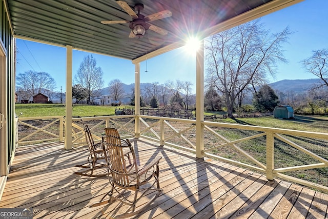 deck with a mountain view, ceiling fan, a storage shed, and a lawn