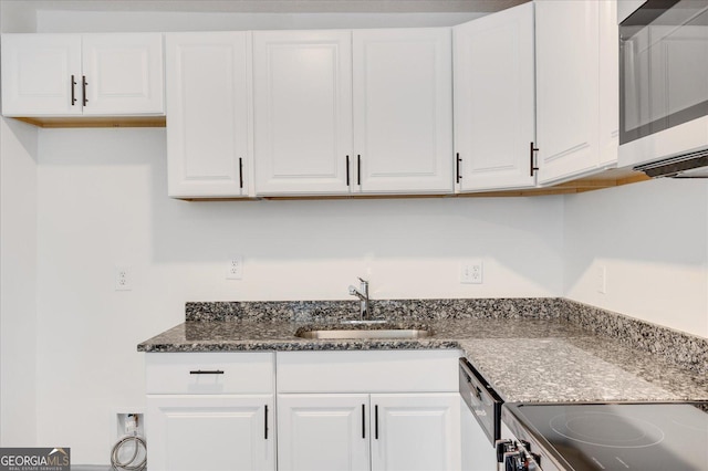 kitchen with dishwasher, dark stone countertops, white cabinetry, and sink