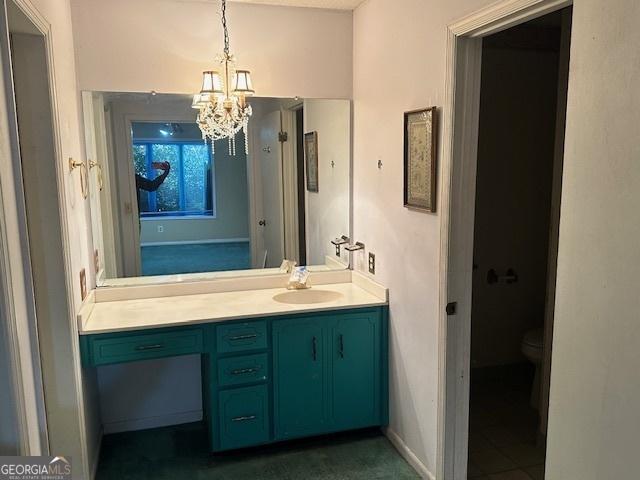 bathroom with toilet, an inviting chandelier, baseboards, and vanity