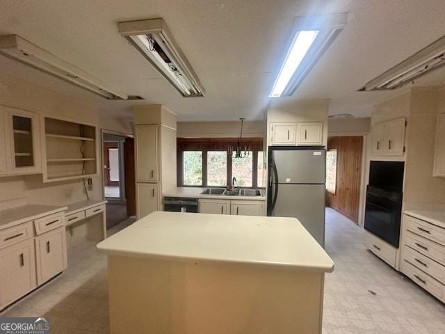 kitchen with glass insert cabinets, a center island, light countertops, black appliances, and a sink