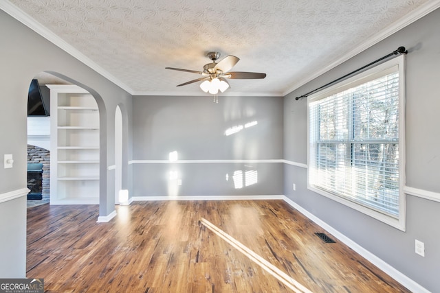 empty room featuring a wealth of natural light, crown molding, and wood-type flooring