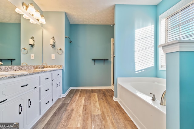 bathroom with hardwood / wood-style flooring, vanity, a bath, and a textured ceiling