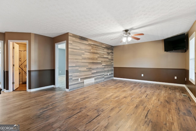 spare room featuring ceiling fan, wooden walls, wood-type flooring, and a textured ceiling