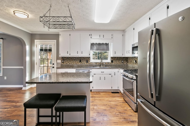 kitchen with stainless steel appliances, a kitchen island, dark stone counters, a textured ceiling, and white cabinets