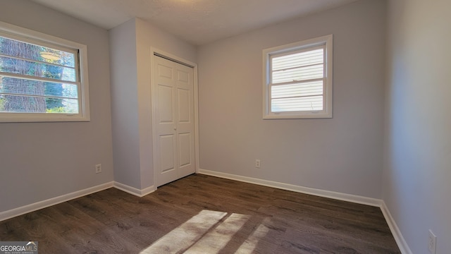 unfurnished bedroom with dark hardwood / wood-style flooring, a closet, and multiple windows