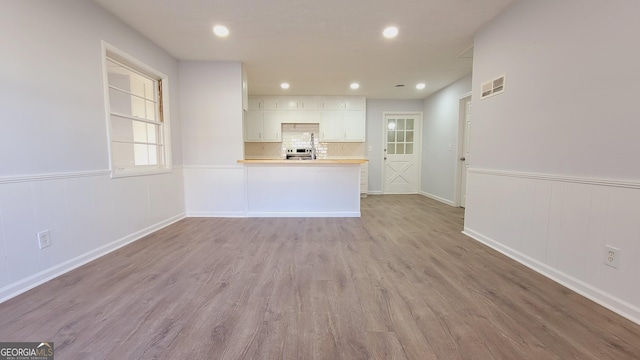 kitchen with kitchen peninsula, decorative backsplash, stainless steel range, light hardwood / wood-style floors, and white cabinetry