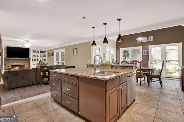 kitchen with light stone counters, built in shelves, a sink, a stone fireplace, and stainless steel dishwasher