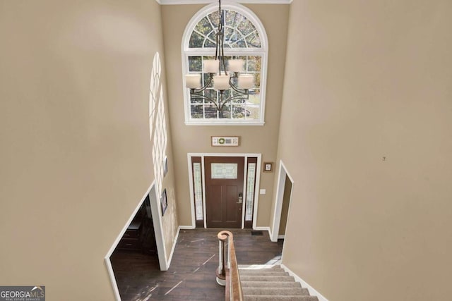 entryway featuring dark wood-type flooring, stairway, an inviting chandelier, baseboards, and a towering ceiling